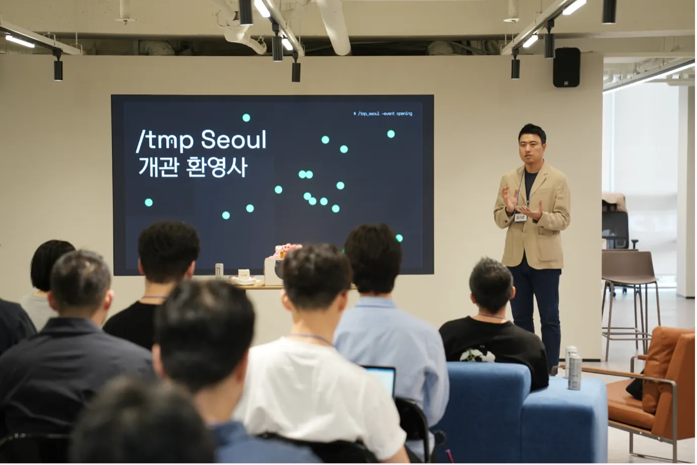 템프서울 개관 행사. 앞쪽 화면에 /tmp Seoul 개관 환영사라는 글자가 떠 있고, 오른쪽에 선 카카오벤처스 김기준 대표가 이야기하고 있다. 참석자들은 뒷모습으로 앉아 있고 벽 쪽에 높은 의자와 소파가 있다